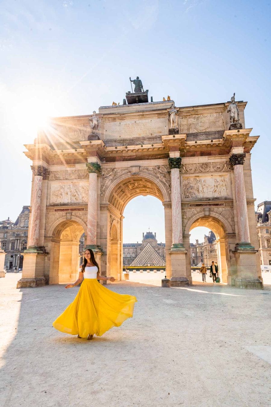 Girl in a yellow skirt twirling in front of Arc de Triomphe du Carrousel in Paris