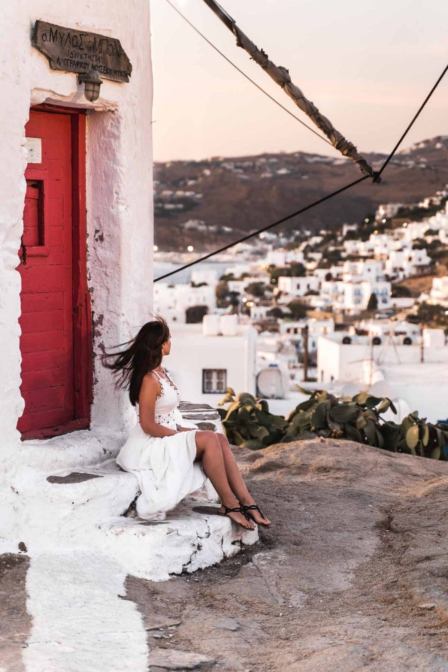 Girl in a white dress standing in front of Boni's Windmill, watching the sunset over Mykonos Town