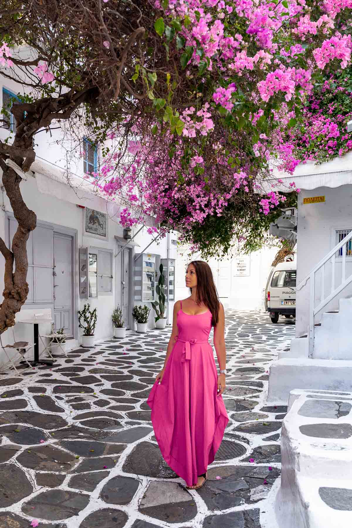 Girl in a pink dress standing under a huge pink bougainvillea tree in Mykonos