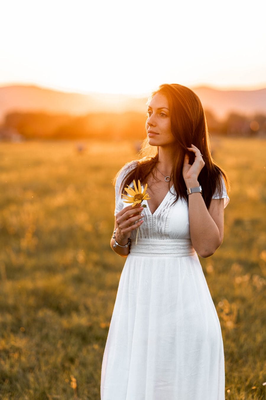 Girl in a white dress standing on a field at sunset