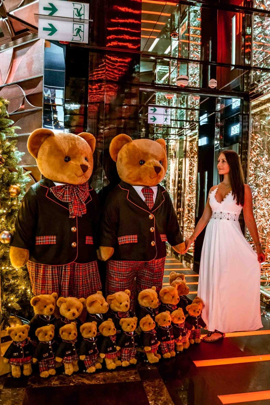 Girl in a white dress holding hands with a stuffed bear which is a part of the Christmas decoration