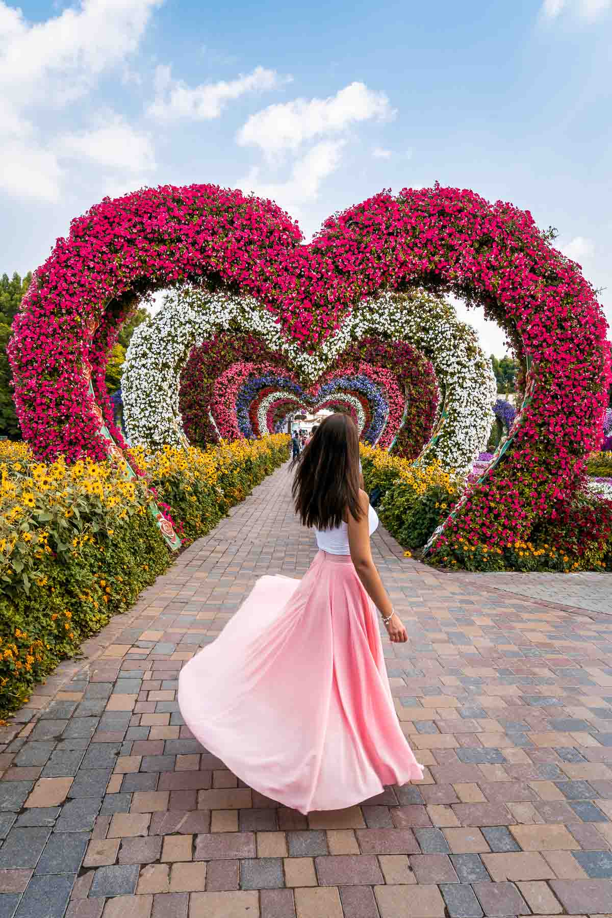 Girl in a pink skirt twirling in front of a pink heart shaped tunnel in the Dubai Miracle Garden