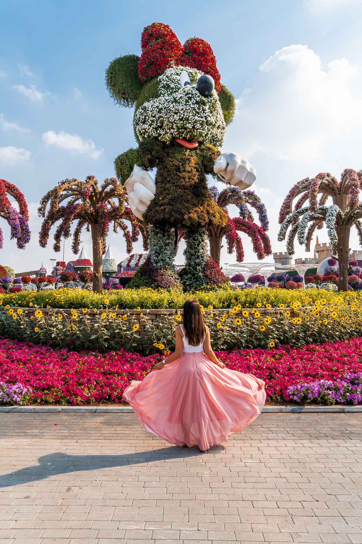 Girl in a pink flowy skirt standing in front of a huge Minnie statue made of flowers in the Dubai Miracle Garden