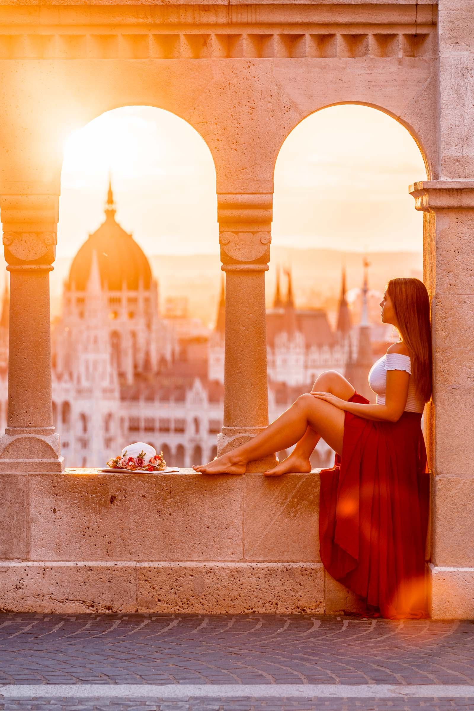 Girl in a red dress sitting at a viewpoint at the Fisherman's Bastion, looking at the Hungarian Parliament at sunrise