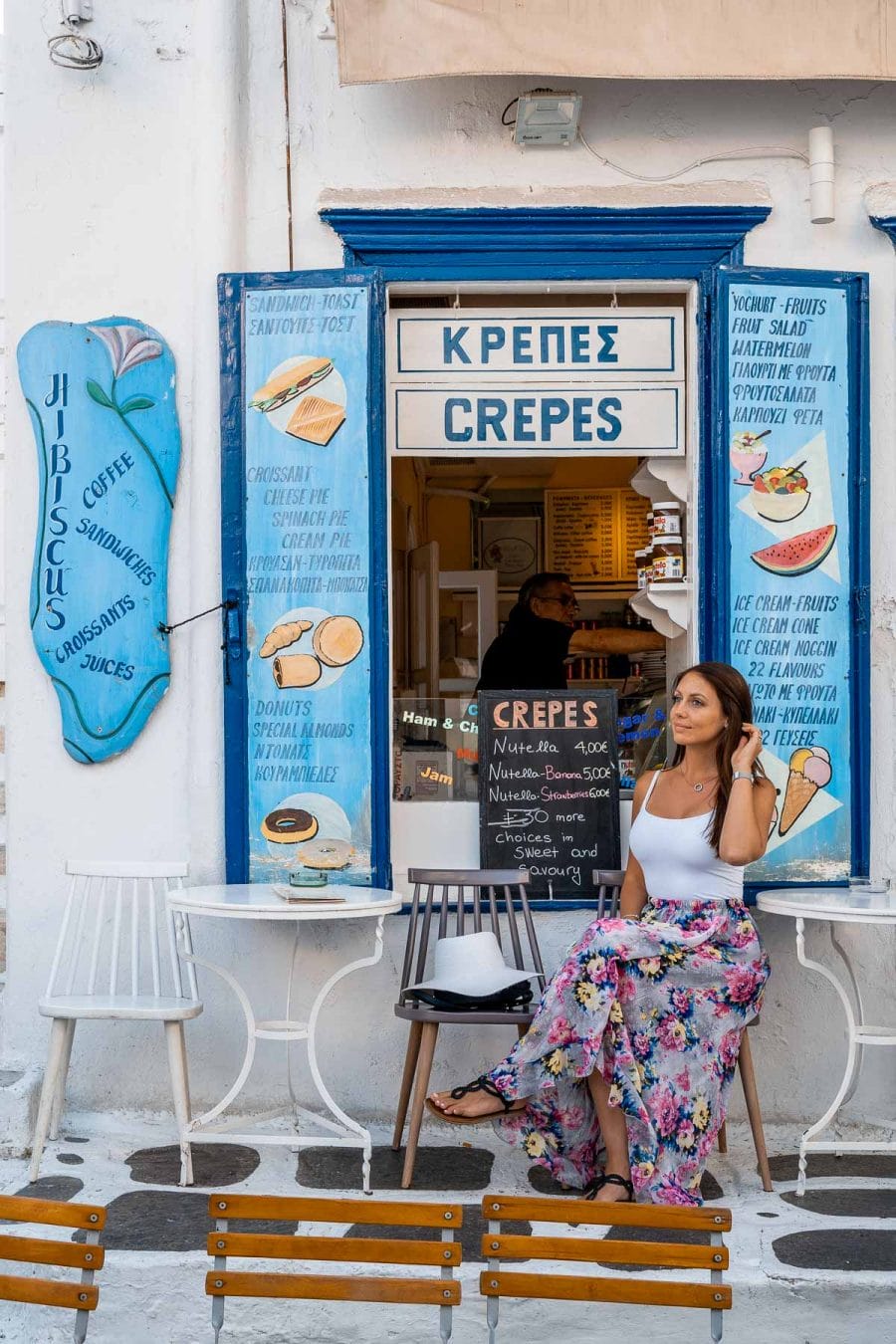 Girl in a purple floral dress sitting in front of the Hibiscus Fruit Parlor in Mykonos