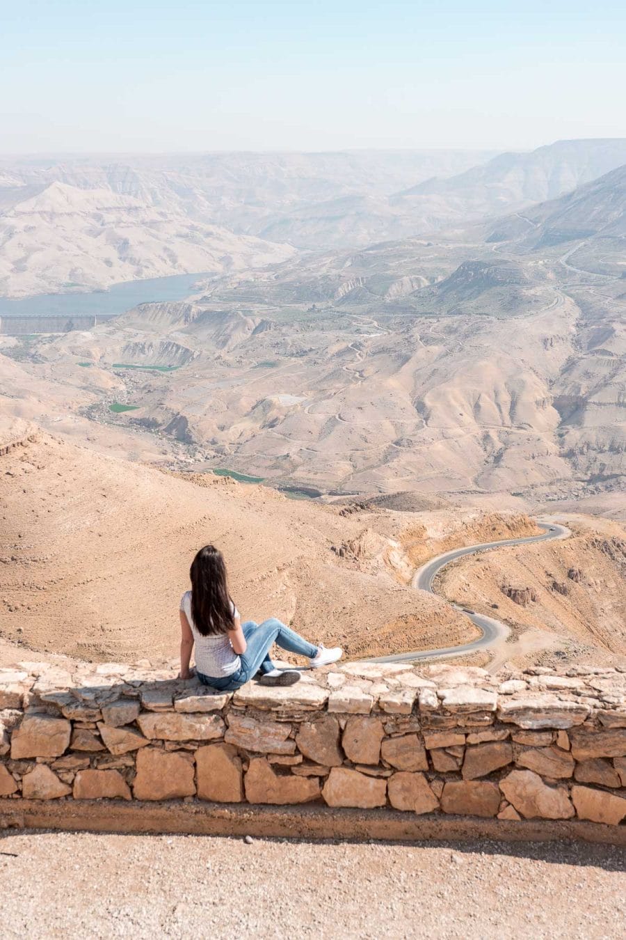 Girl in a white T-shirt and jeans looking at the winding roads of the King's Highway in Jordan