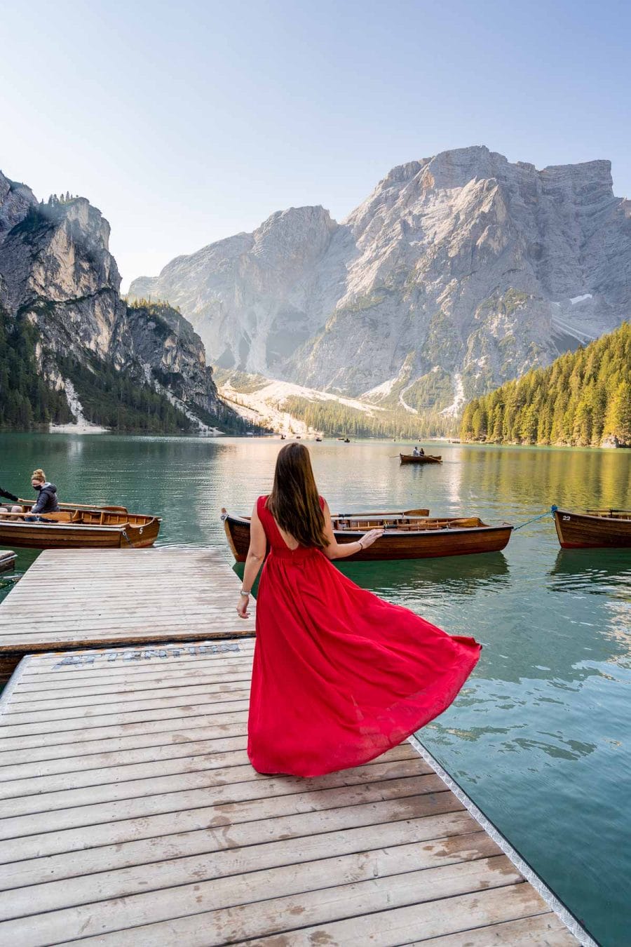 Girl in a red dress standing on the pier at Lago di Braies, which is a must visit on every Dolomites road trip itinerary