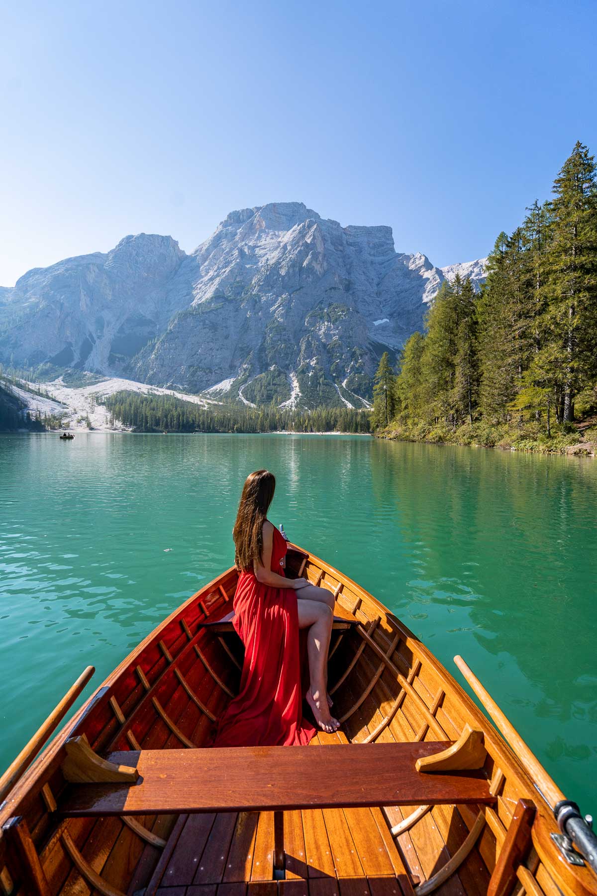 Girl in a red dress sitting in a rowboat at Lago di Braies in the Dolomites
