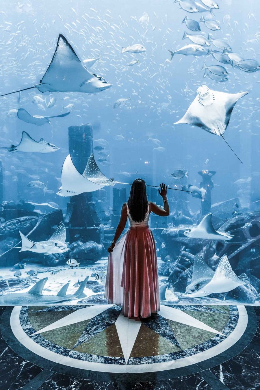 Girl in pink skirt standing in front of a huge aquarium at the Atlantis hotel in Dubai