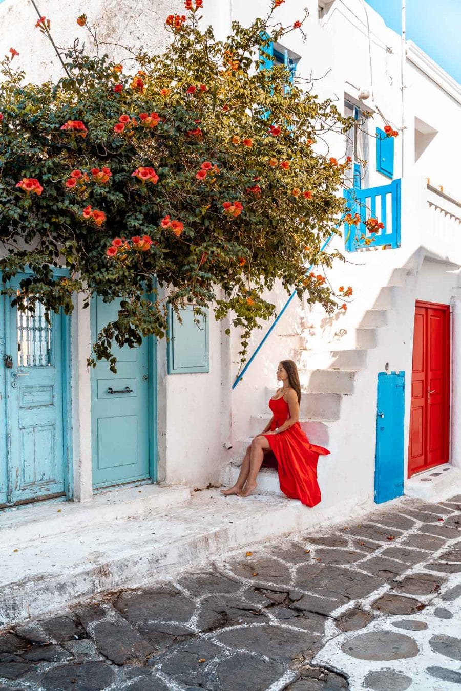 Girl in a red dress sitting on a stair at the turquoise door in Mykonos
