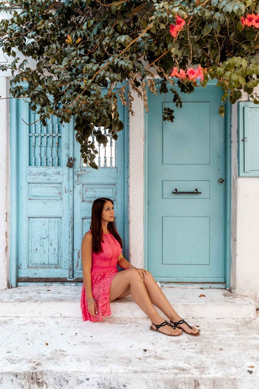 Girl in a pink dress sitting in front of a turquoise door in Mykonos