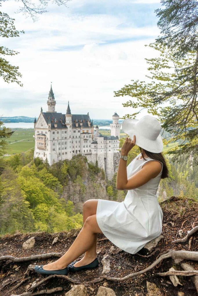 Girl in a white dress sitting at the secret viewpoint at Neuschwanstein Castle