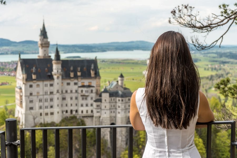 Girl in a white dress looking at the Neuschwanstein Castle from a viewpoint