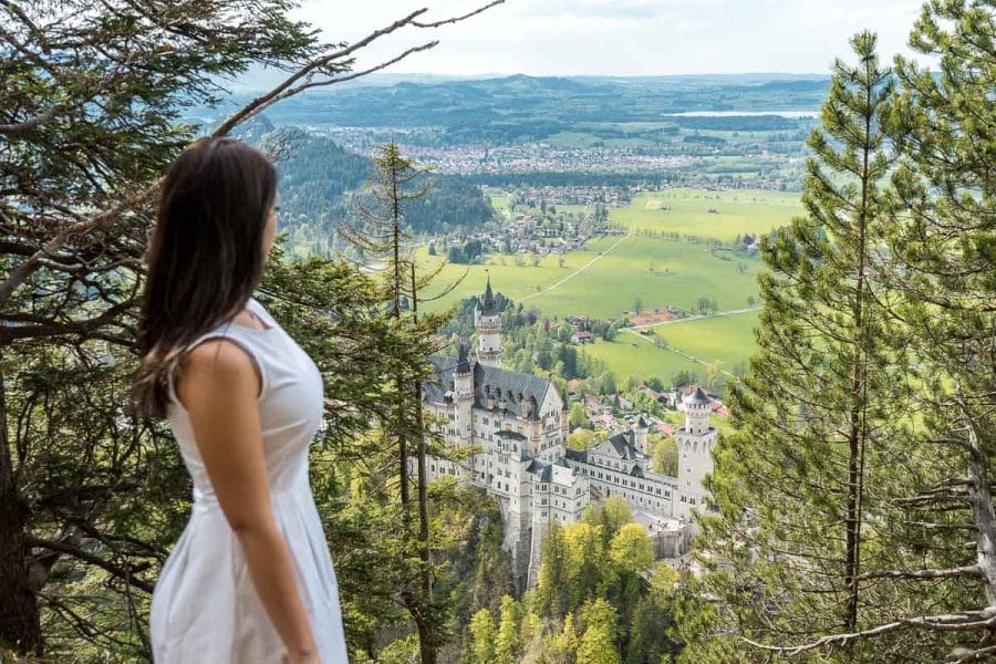 Girl in a white dress looking at the Neuschwanstein Castle from an upper viewpoint