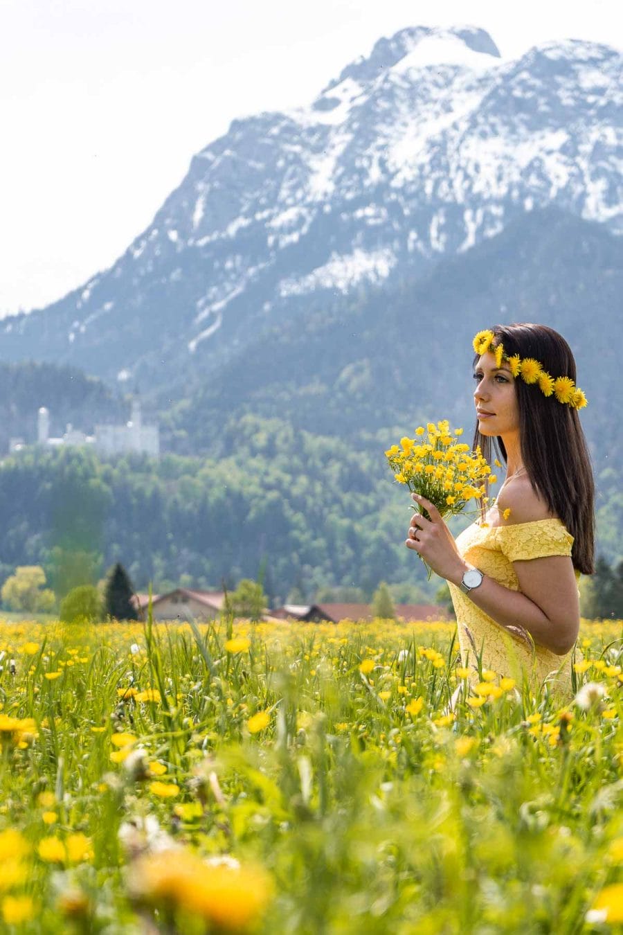 Girl in a flower crown sitting in a daffodil field with the Neuschwanstein Castle in the background