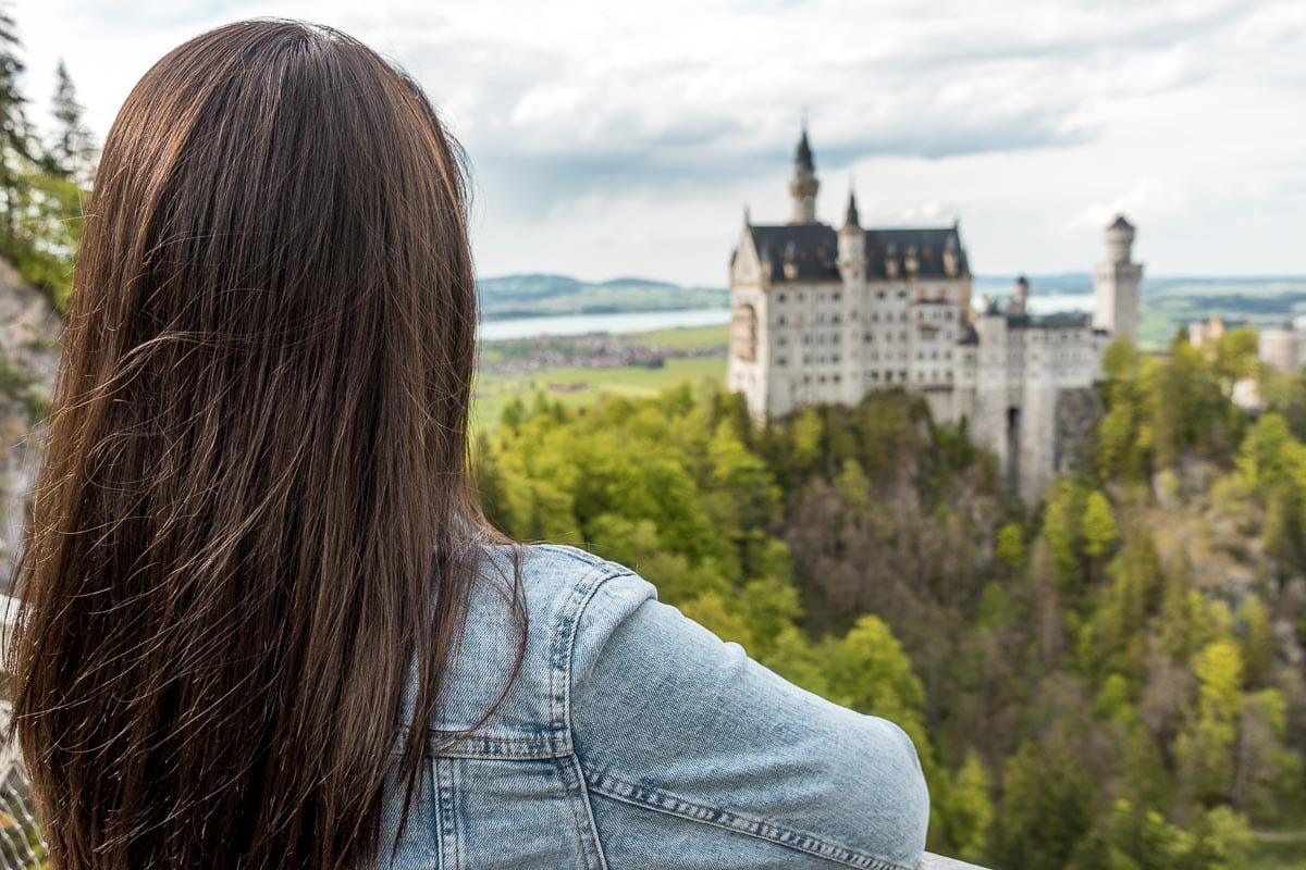 Girl in a denim jacket looking at the Neuschwanstein Castle from the Marienbrücke