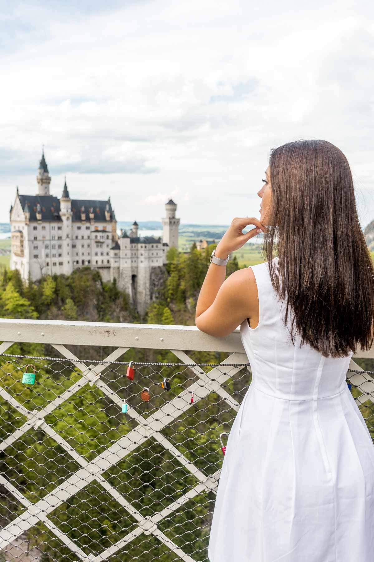 Girl in a white dress looking at the Neuschwanstein Castle from the Marienbrücke