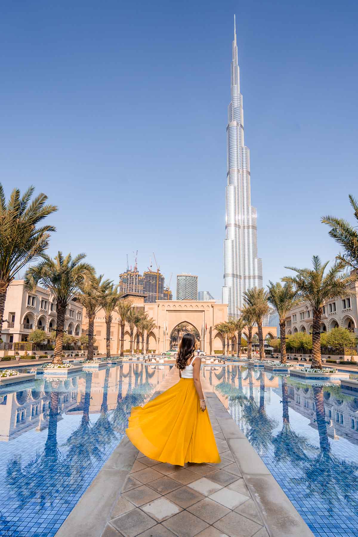 Girl in yellow skirt twirling in front of the Palace Downtown in Dubai with the Burj Khalifa in the background