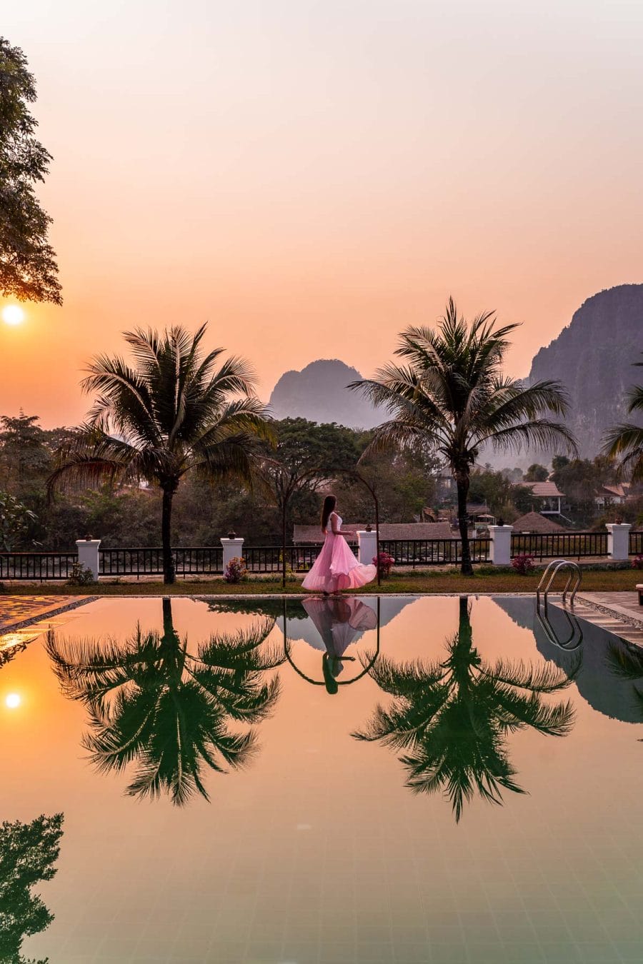 Girl in a pink dress standing at the pool in Riverside Boutique Resort Vang Vieng during sunset