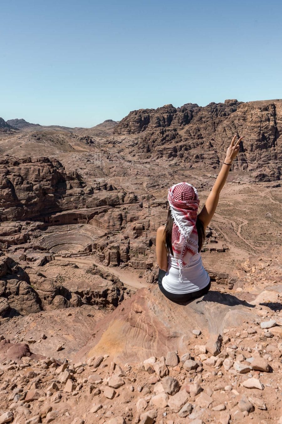 Girl in a white top and a white-red keffiyeh looking at the Nabatean ruins in Petra, Jordan