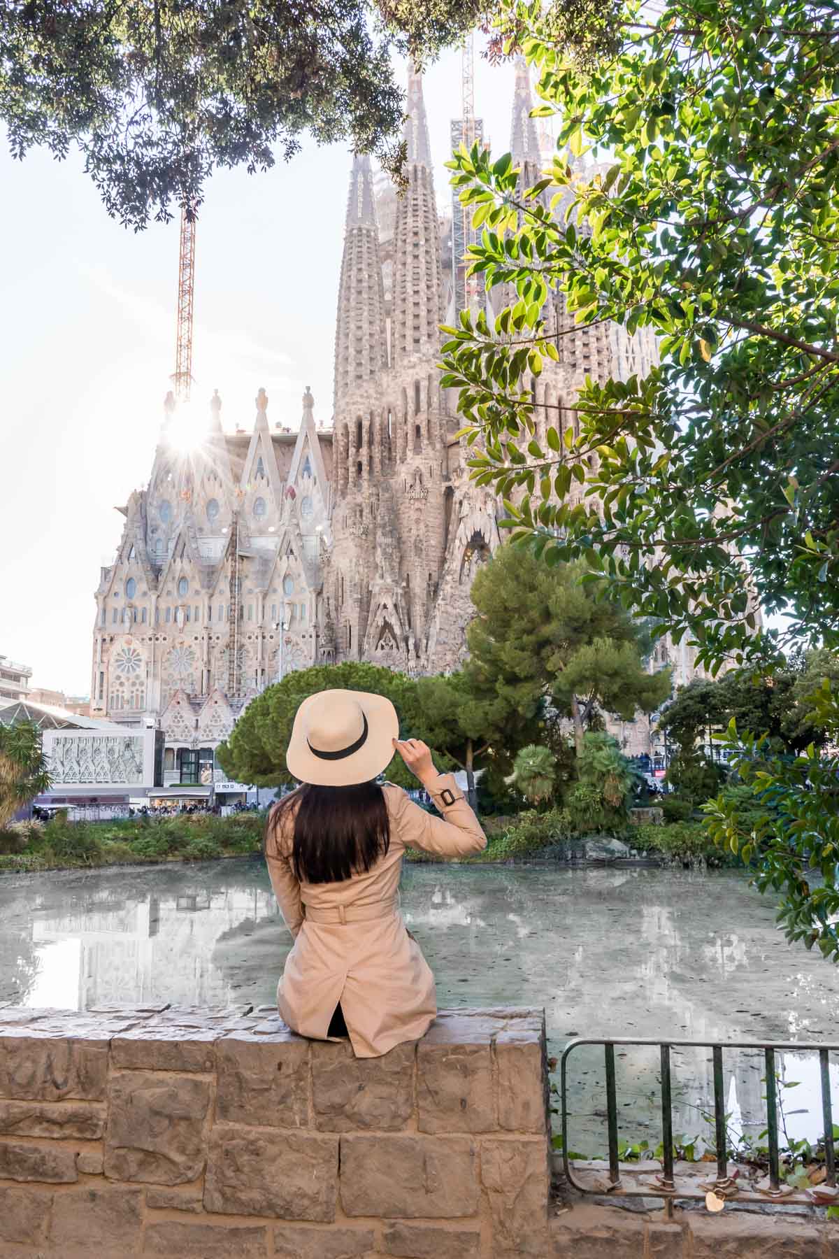 Girl in a hat and a trench coat sitting in front of the Sagrada Familia in Barcelona
