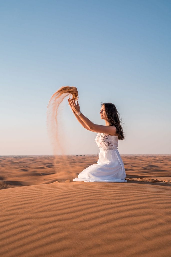 Girl in a white dress throwing sand in the air in the Dubai desert