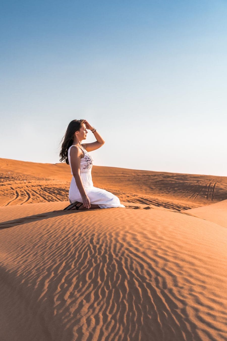 Girl in white dress sitting in the Dubai desert on the sand dunes
