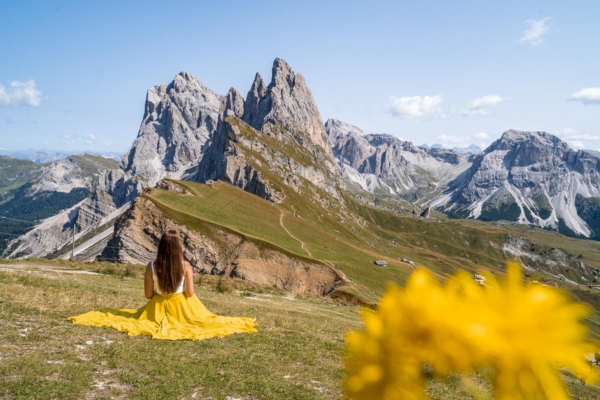 Girl in a yellow skirt sitting at Seceda ridgeline in the Dolomites, Italy