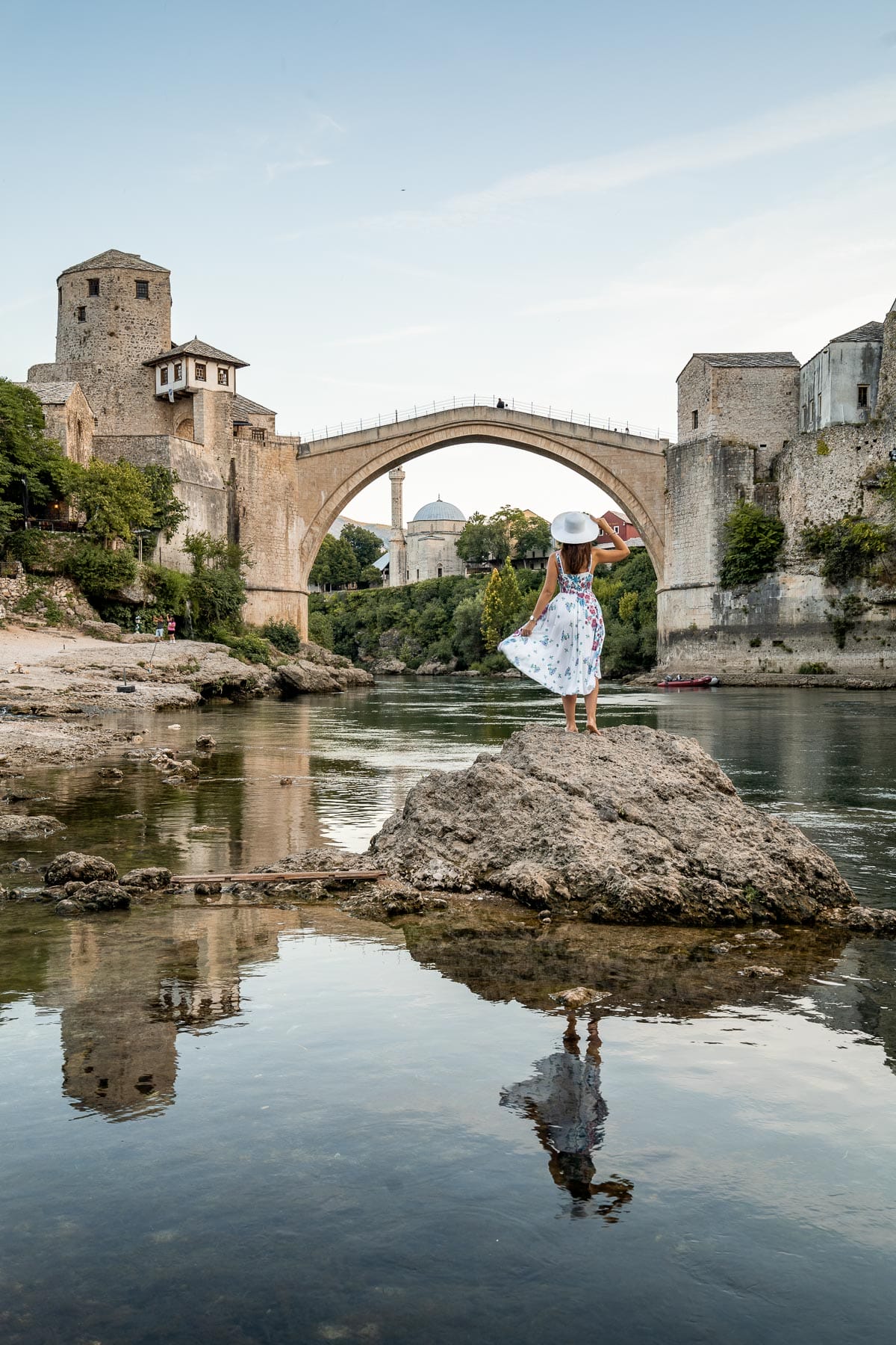 Girl in a floral dress standing on a rock in front of the Stari Most Old Bridge in Mostar, Bosnia-Herzegovina