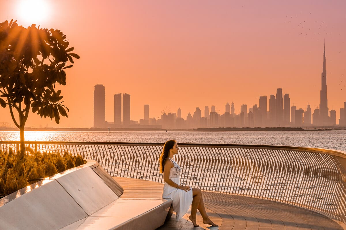 Girl in a white dress sitting at the Dubai Creek Harbour at sunset which is one of the most instagrammable places in Dubai