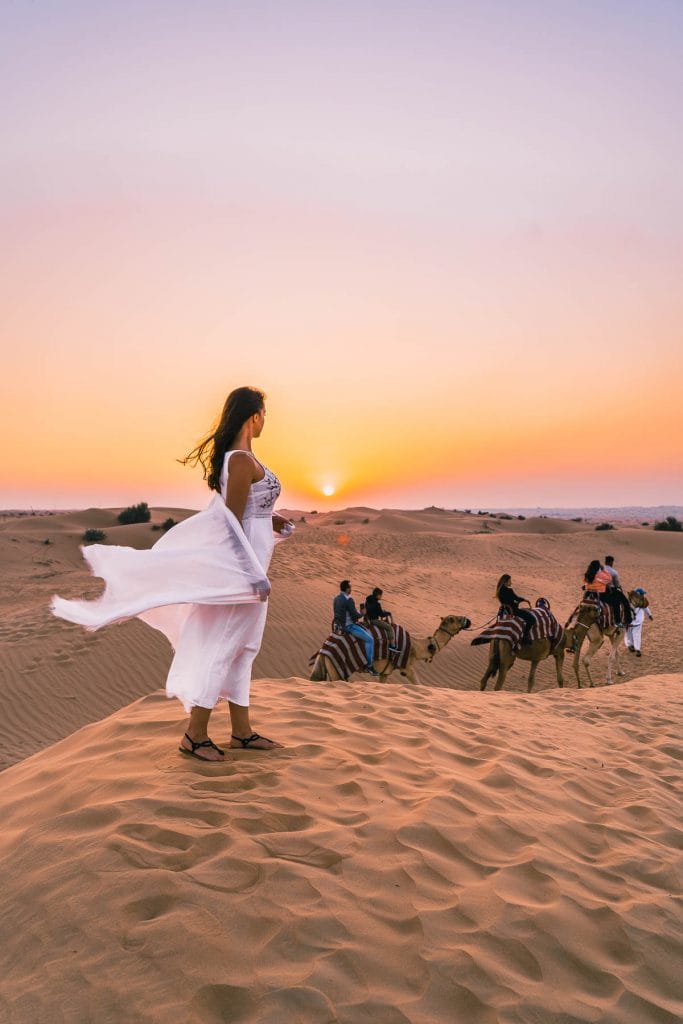 Sunset view in the Dubai desert with a girl in white dress standing in the sand dunes