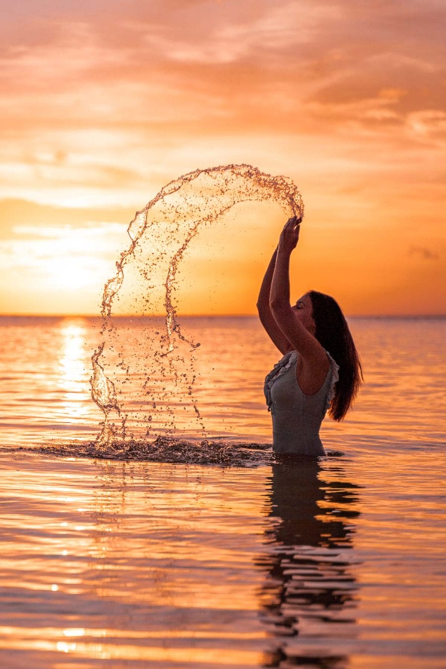 Girl throwing water up in the air in the ocean at sunset in Siquijor, Philippines
