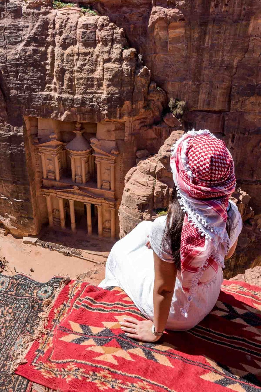 Girl in a white dress and a white-red keffiyeh sitting at the best Treasury viewpoint in Petra, Jordan