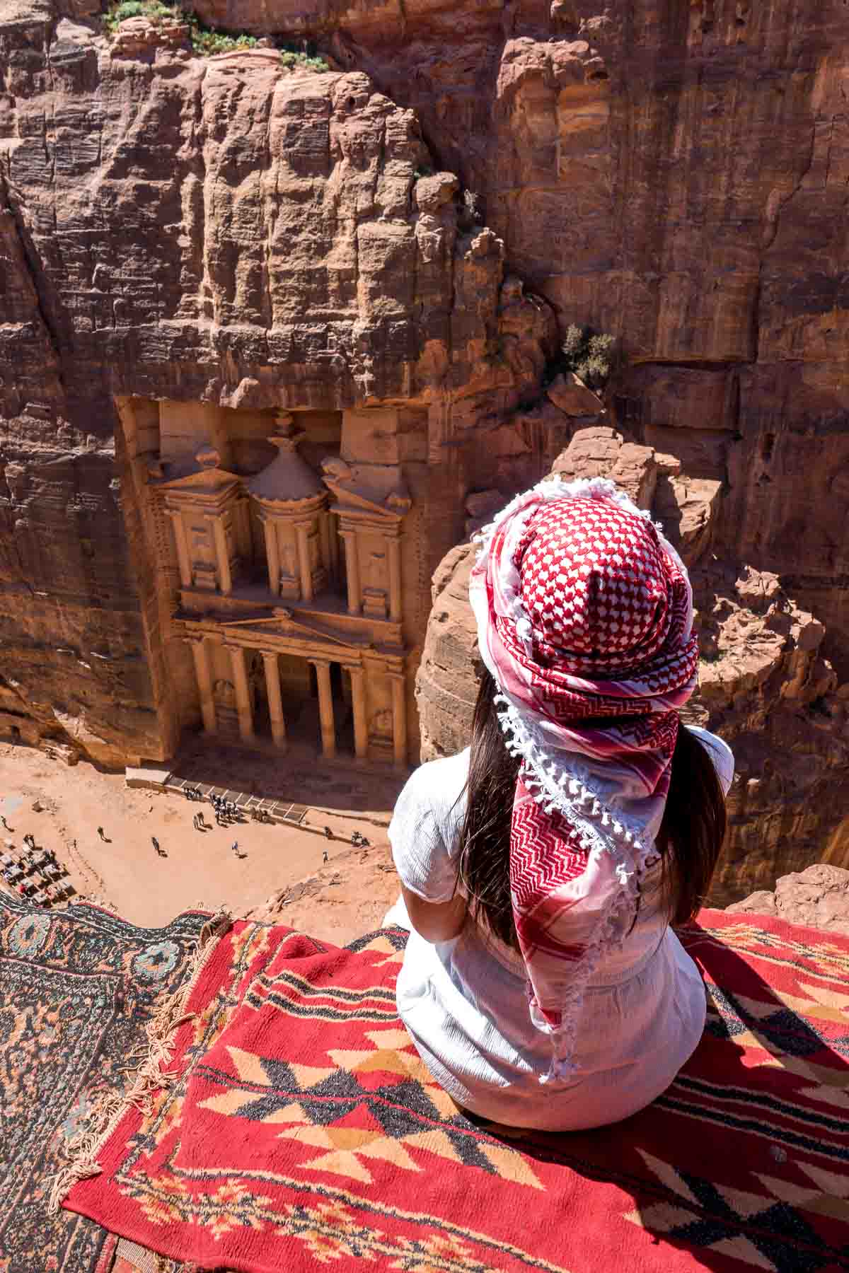 Girl in a white dress and a white-red keffiyeh sitting at the best Treasury viewpoint in Petra, Jordan