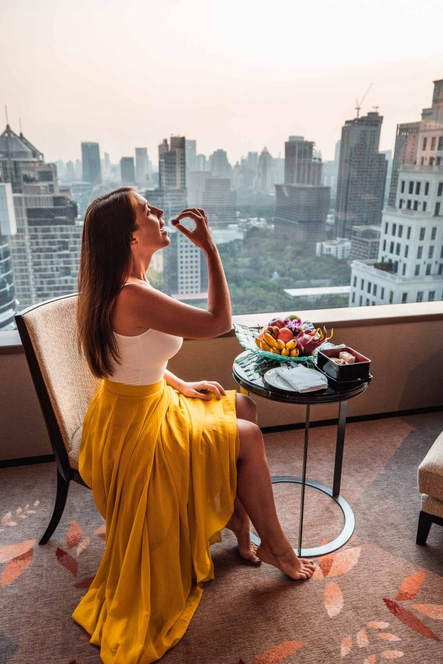 Girl in a yellow skirt sitting in one of the rooms of The Okura Prestige Bangkok enjoying the view