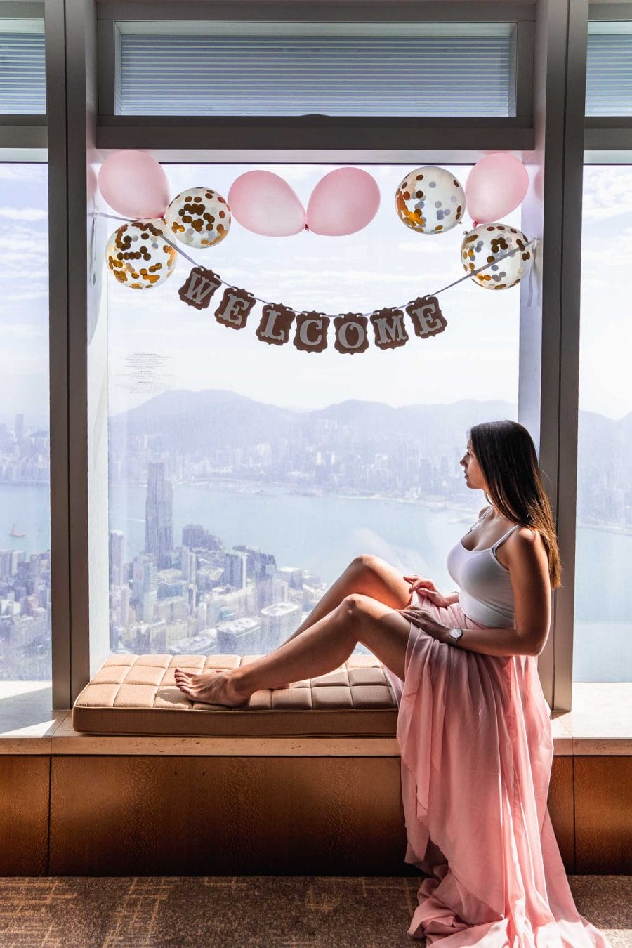 Girl in pink skirt sitting in the window looking over the Victoria Harbour in Hong Kong