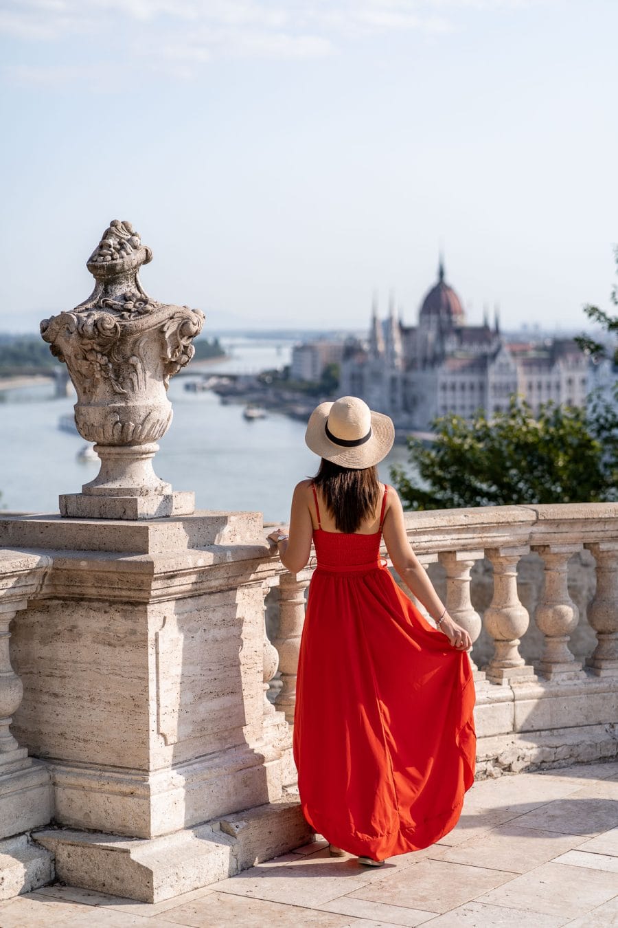 Girl in a red dress standing at the Buda Castle with the Hungarian Parliament in the background