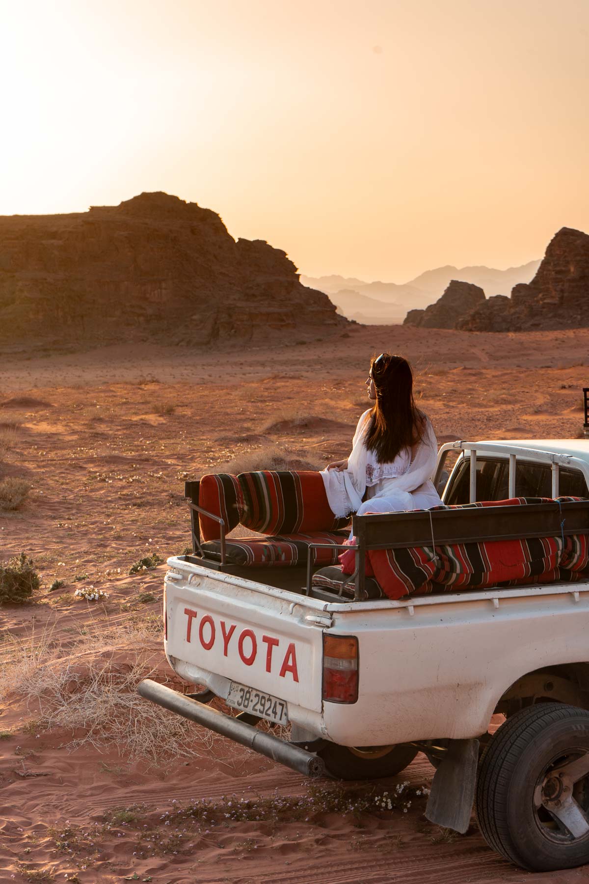 Girl in a white dress watching the sunset in a pick-up truck in the Wadi Rum, Jordan