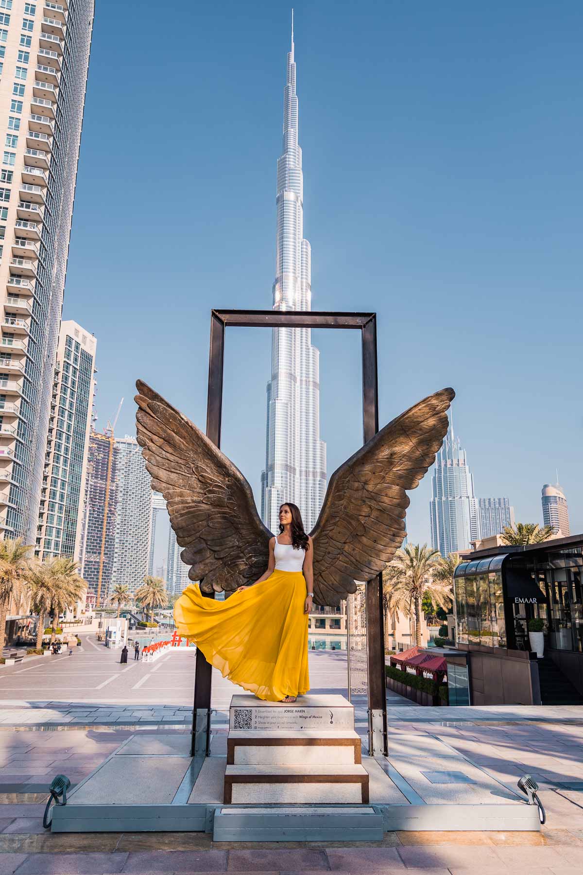 Girl in yellow skirt doing a skirt flip in front of the Wings of Mexico in Dubai with the Burj Khalifa in the background