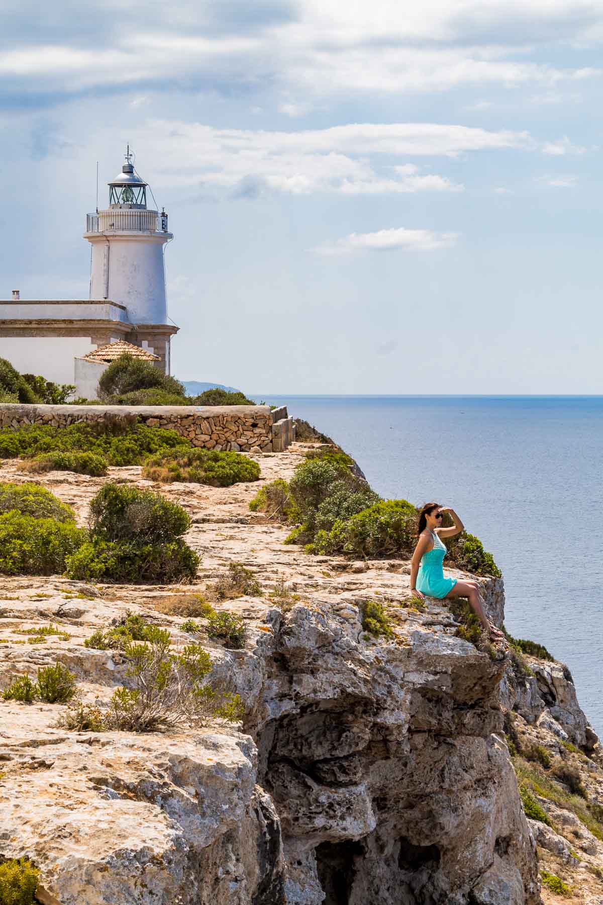 Girl in a blue dress sitting in front of Far de Cap Blanc lighthouse in Mallorca