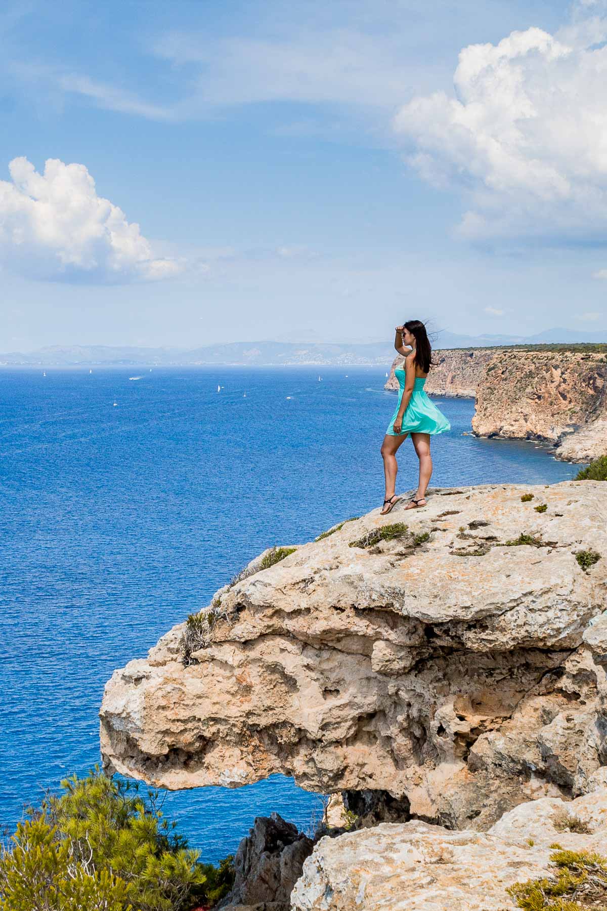 Girl in a blue dress standing on a rock at the coastline of Mallorca