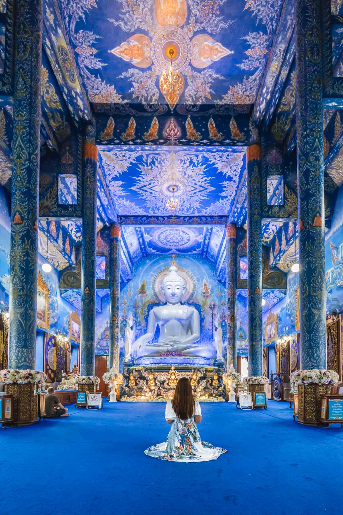 Girl in a blue dress sitting in front of a white Buddha statue in the Blue Temple in Chiang Rai