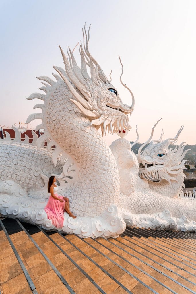 Girl in a pink skirt sitting on a dragon statue at Huay Pla Kang Temple in Chiang Rai