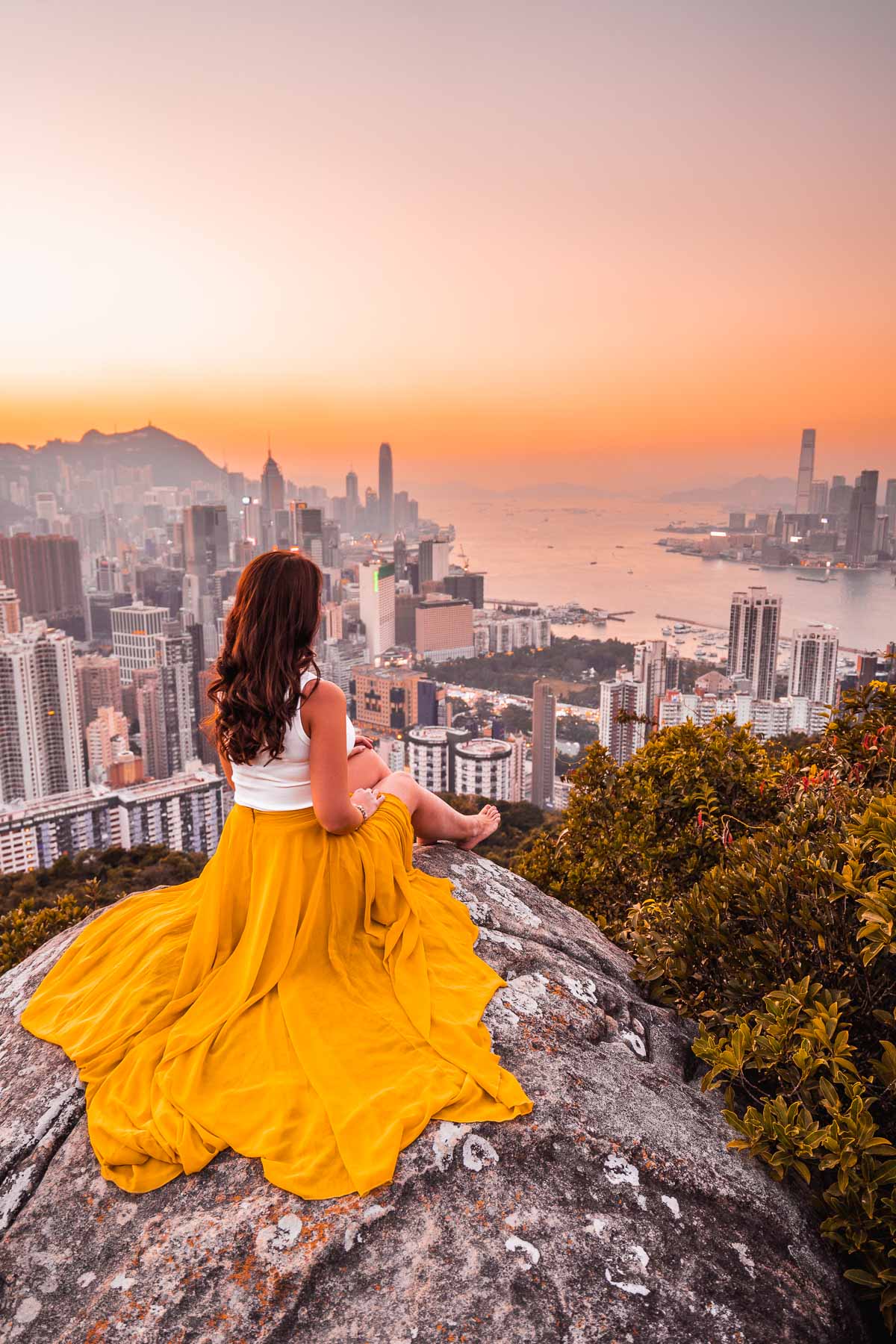 Girl in a yellow skirt sitting on a rock, watching the sunset from Braemer Hill, Hong Kong