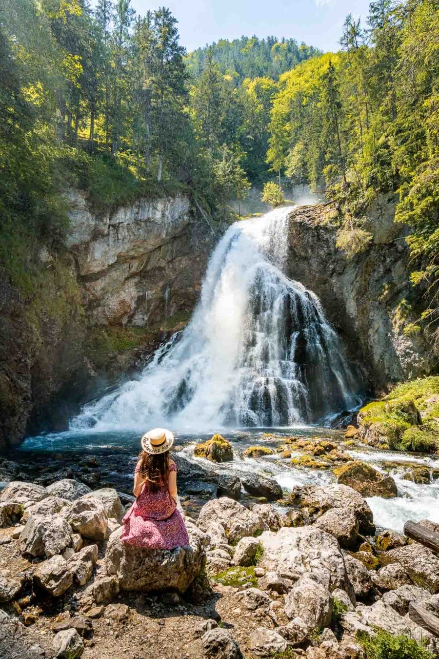 Girl in a red dress sitting in front of Gollinger waterfall, Austria