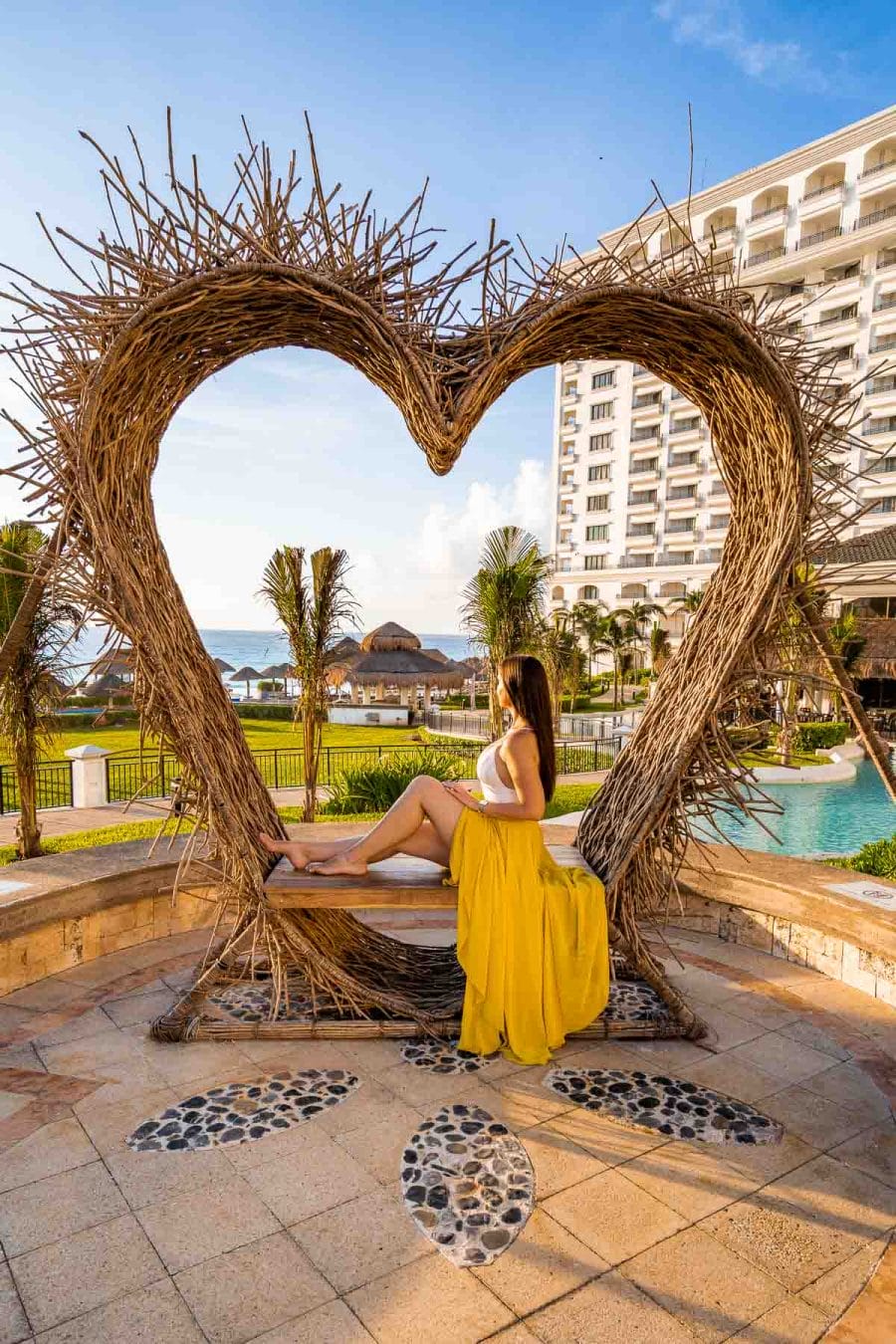 Girl in a yellow skirt sitting in a wooden heart at JW Marriott Cancun