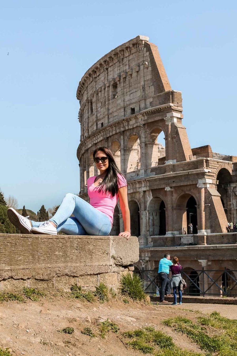 Girl in a pink skirt sitting in front of the Colosseum in Rome, Italy