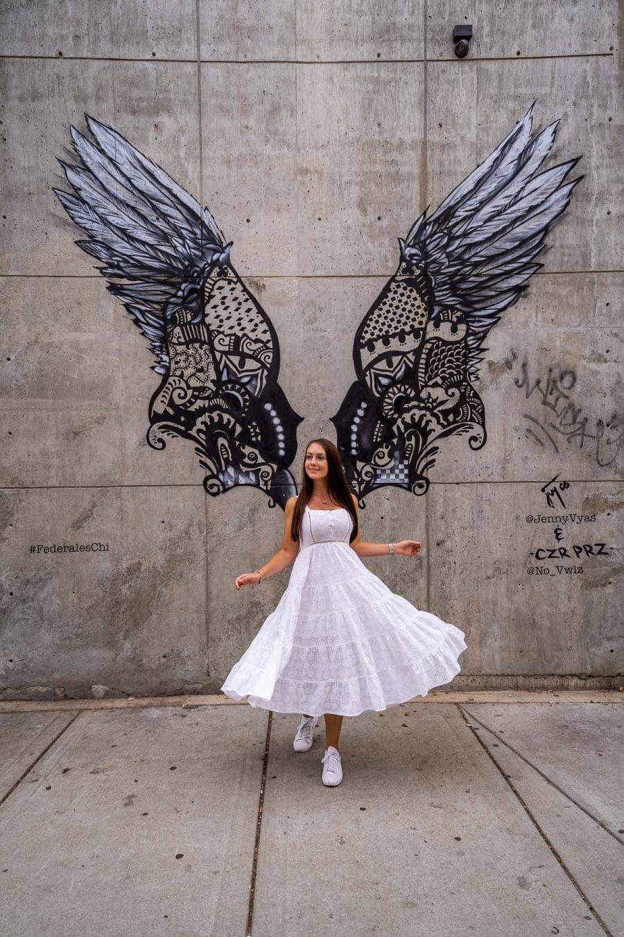 Girl in white dress in front of a Black wing mural in Chicago