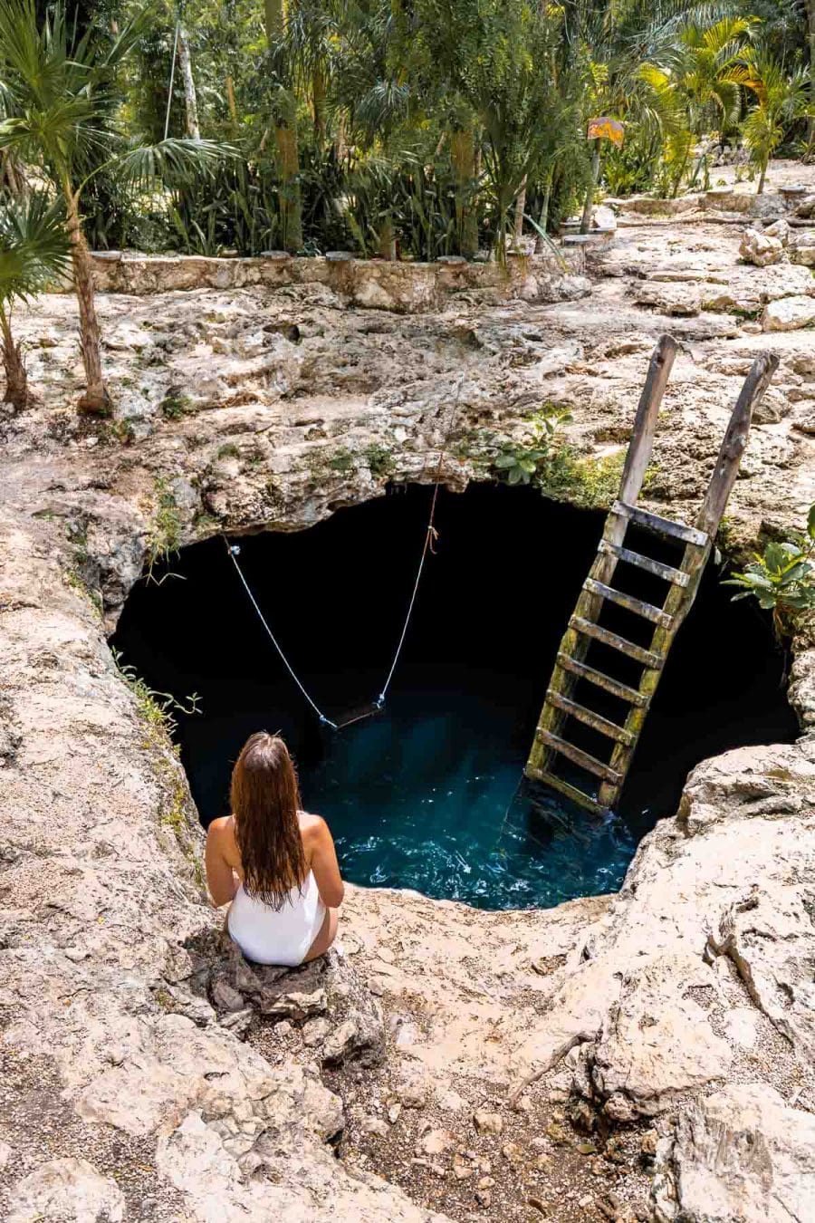 Girl in white swimsuit sitting at Cenote Calavera, a famous photo spot in Tulum