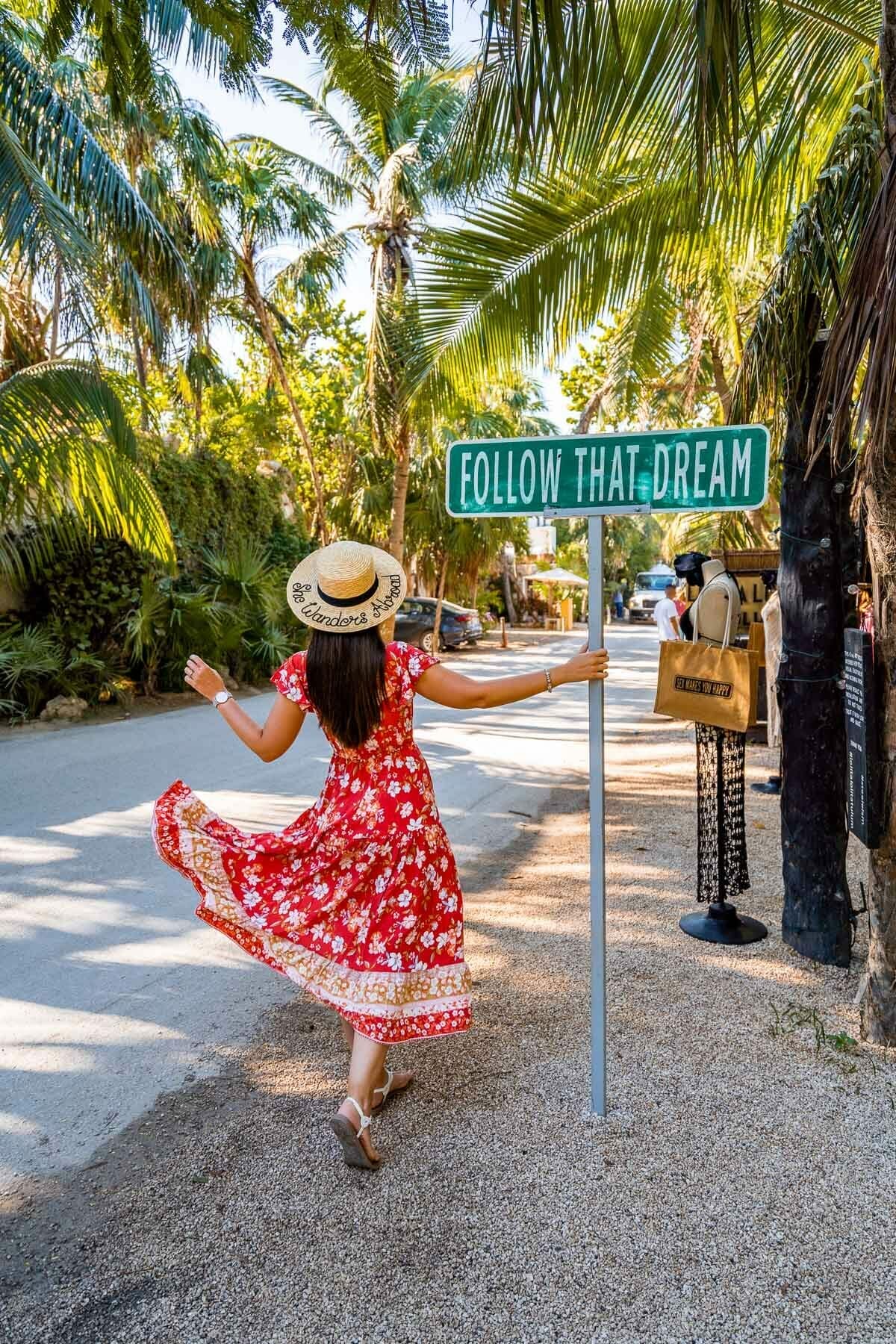 Girl in red dress next to the famous Follow That Dream sign in Tulum, a classic Tulum Instagram spot